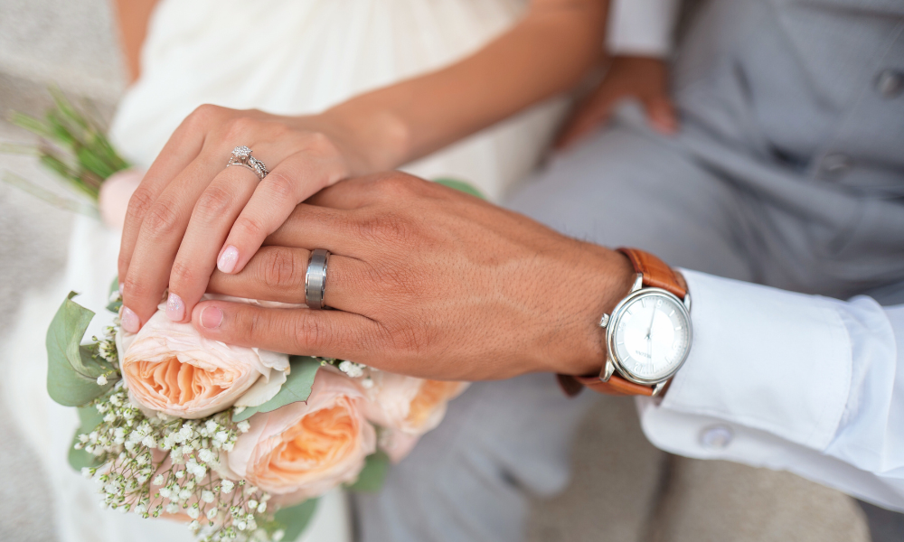 Hands of newlyweds with wedding rings over bouquet of flowers